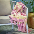 Pink and yellow plaid blanket draped over a white chair with a plant in the background.