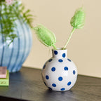 Small white vase with blue polka dots on a wooden surface with a blurred background