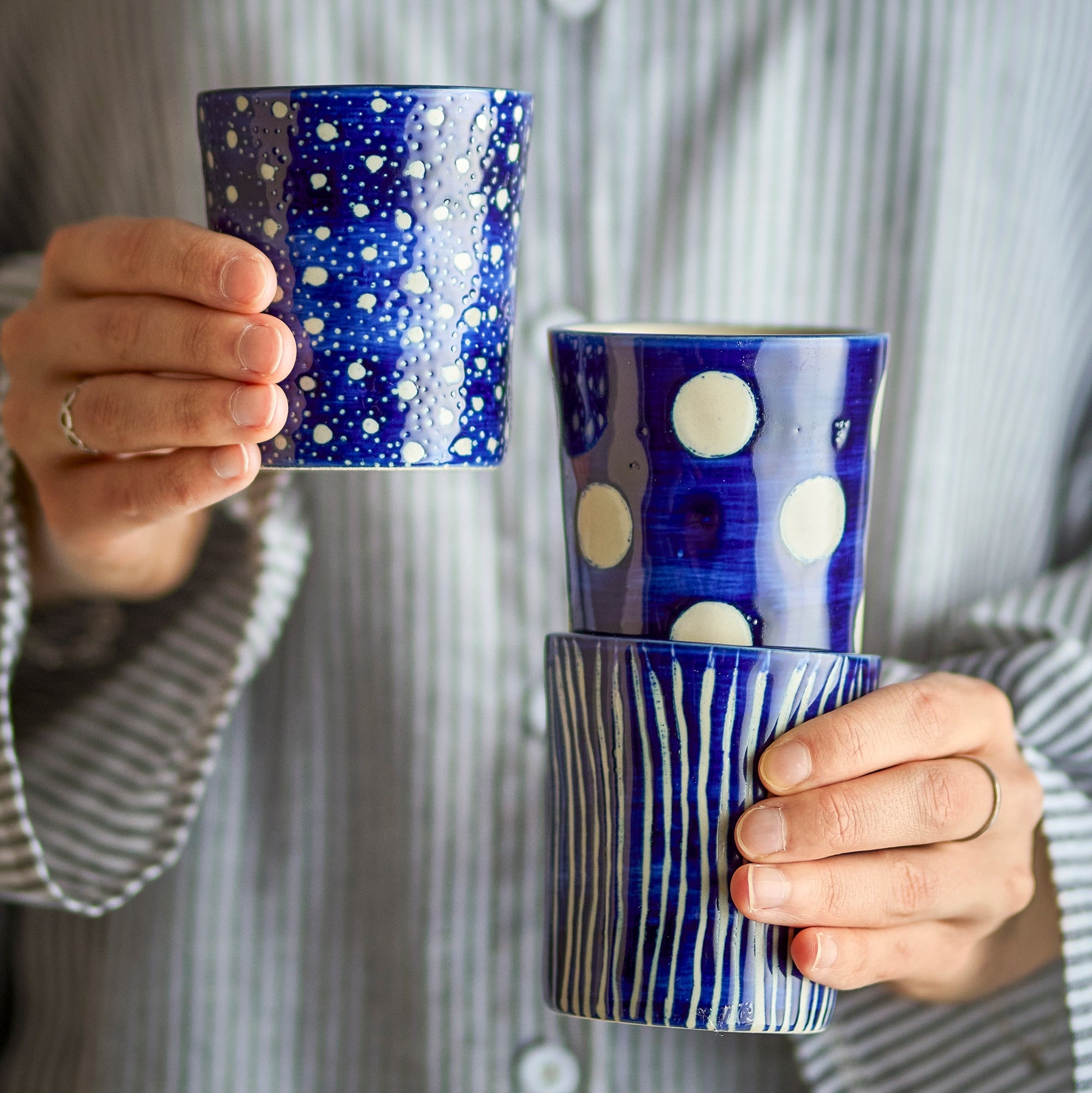 Person holding three blue ceramic mugs with different patterns