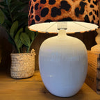 White textured table lamp with a leopard print lampshade on a wooden surface.