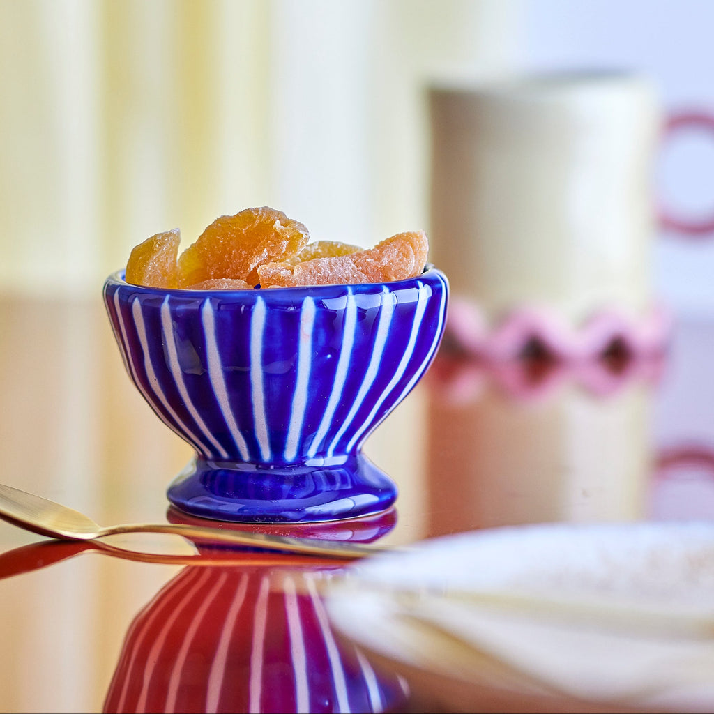 Blue striped bowl with dried fruits on a reflective surface